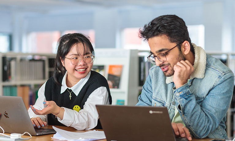 Two students working on laptops whilst talking