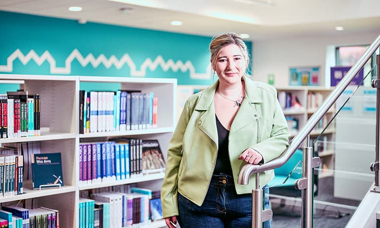 Student standing in front of a library leaning against a stair well