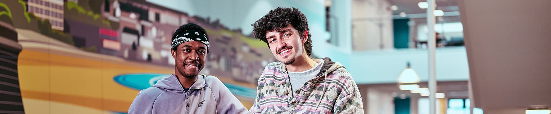 Two male students leaning against a balcony inside a building talking