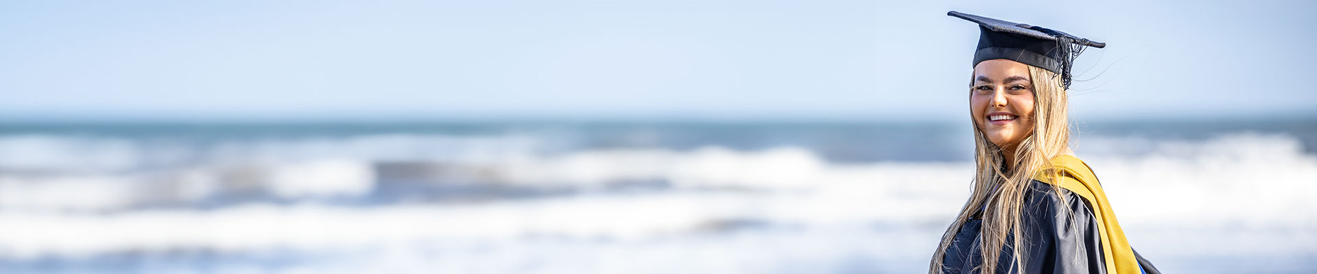 student wearing a graduation rope standing by the sea