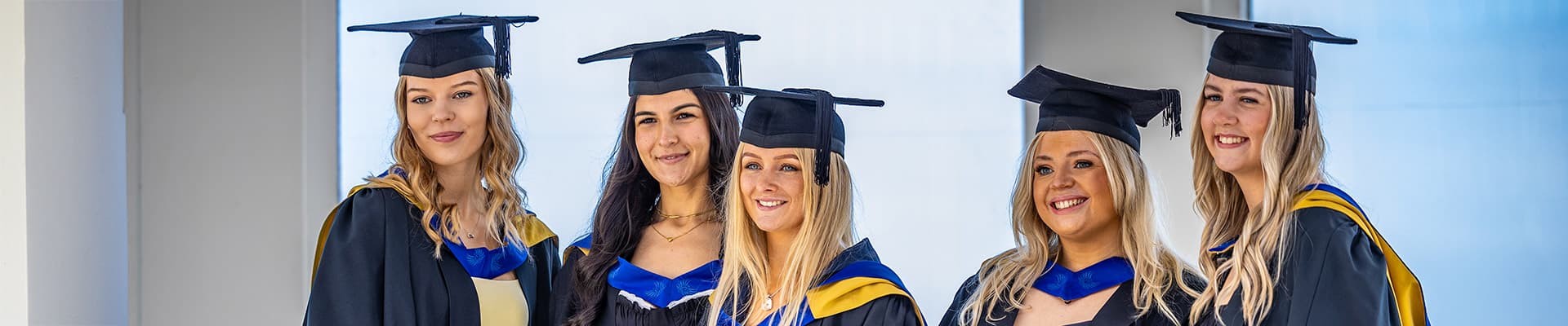 Group of female graduate stood smiling with their graduation gowns and caps