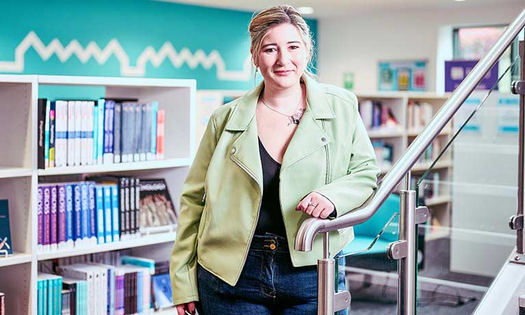 Female leaning against a stairwell standing in front of a library