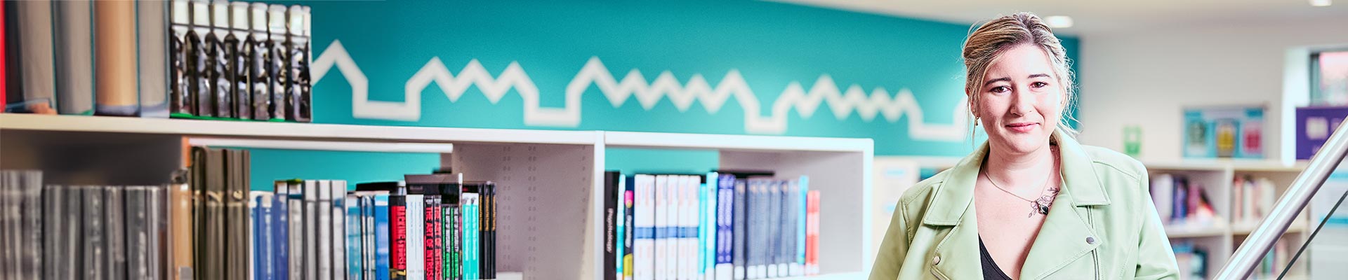 Female student stood in a library with a shelf of books behind