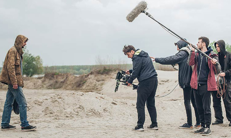 An actor and film crew filming on a sandy beach