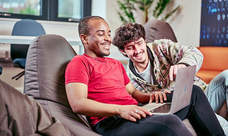 Two male students sat on beanbags looking at a laptop