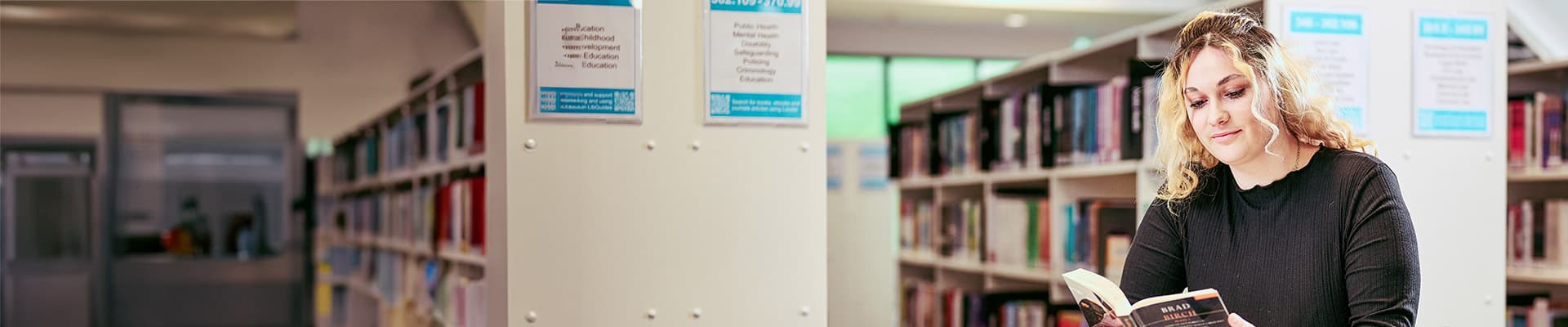 Female student sat in a library reading a book