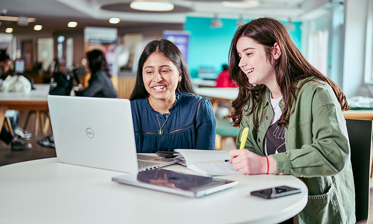 Two students sat at a table looking at a laptop