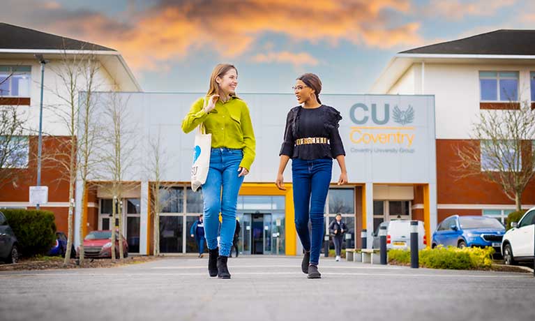 Two students striding out from CU Coventry front door