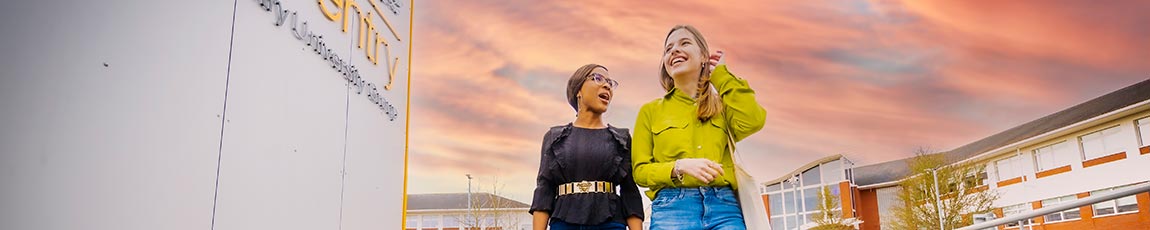 Two students walking past the CUC building with a pink orange sky