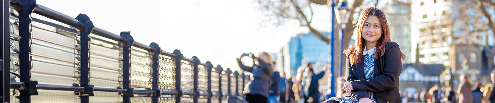 Female student sat on a bench by the River Thames
