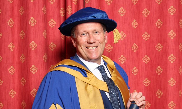 A man smiling dressed in ceremonial robes holding a scroll