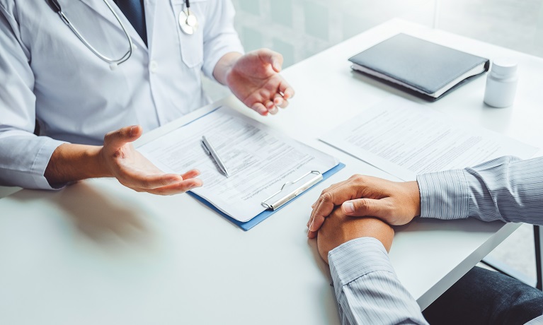 A doctor speaking to a patient across a table with paperwork on the table