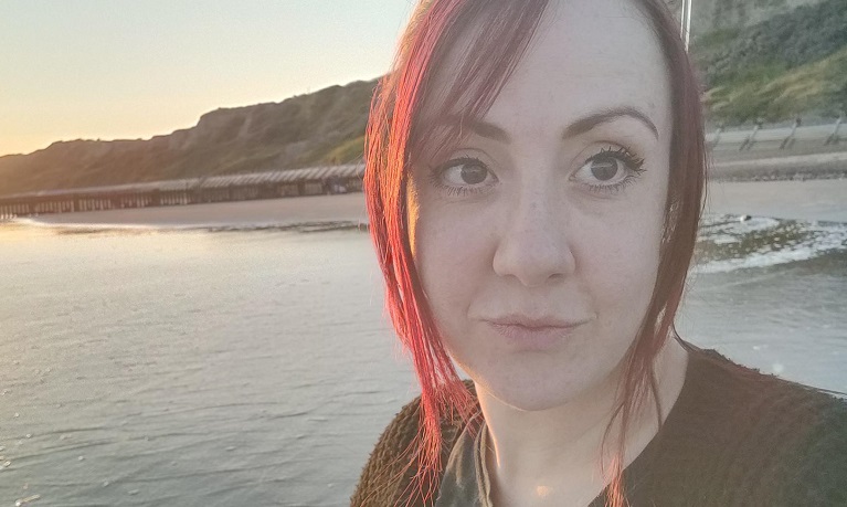 A head and shoulders image of Dr Katherine Hall with a beach in the background