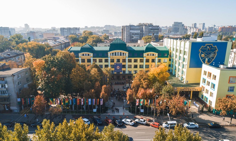 A building of the Alfred Nobel University campus pictured from above with a number of international flags. trees and parked cars in the foreground.