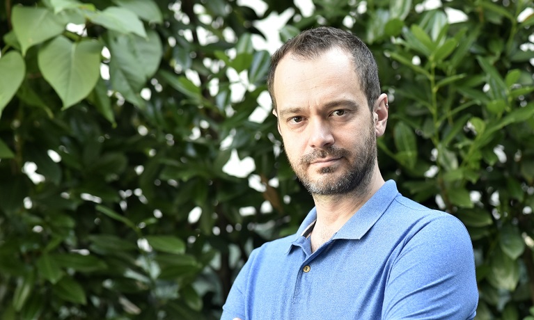 Associate Professor Federico Carollo wearing a blue-t-shirt with green leaves in the background