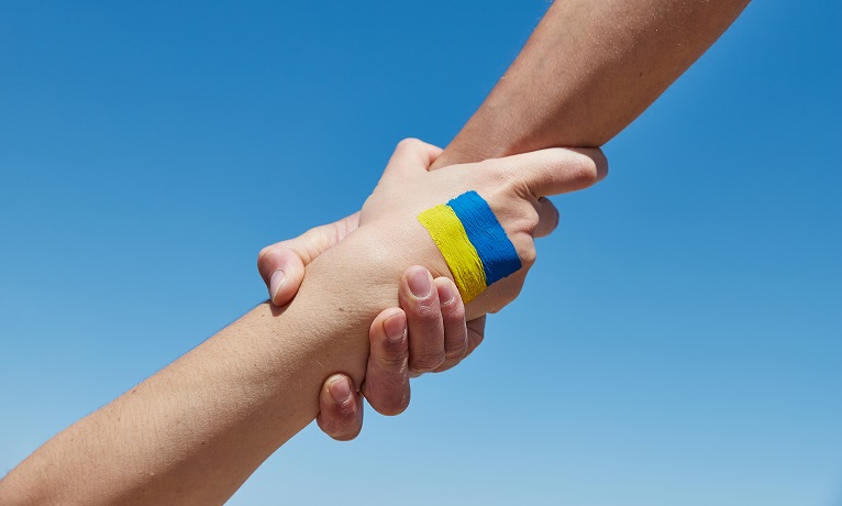 Two hands grasping the other by the wrist with a Ukraine flag painted on the back of one hand