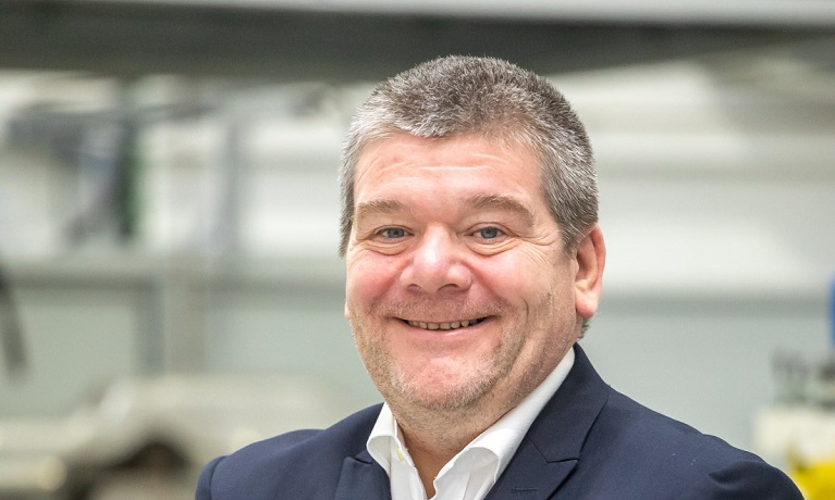 A head and shoulders image of Carl Perrin smiling at the camera while wearing a suit and shirt