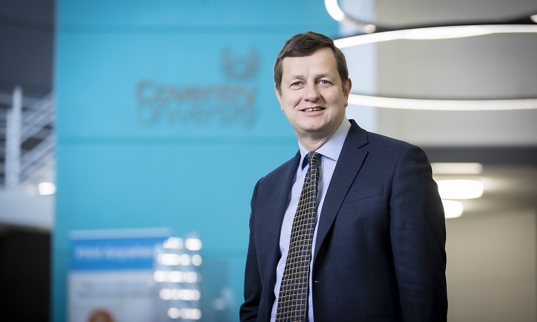 Richard Wells wearing a suit, shirt and tie while smiling at the camera