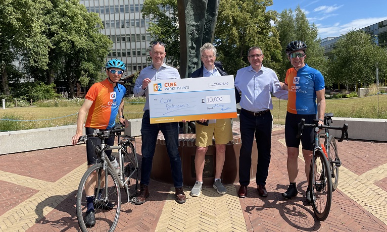 Trevor Cummings, Andy Simons and Mike Ashton from Cure Parkinson’s, Clive Winters from Coventry University and Phill Robinson standing in the sunshine with a cheque for £10,000