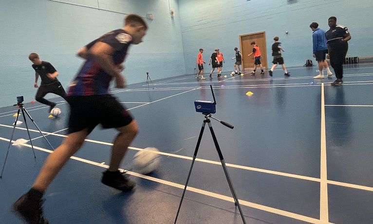 A young footballer running with a football at his feet between two sensors in a sports hall