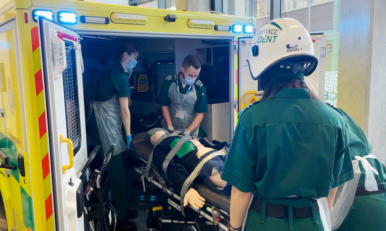 Paramedic students wearing protective equipment treating a mock casualty in a simulated ambulance