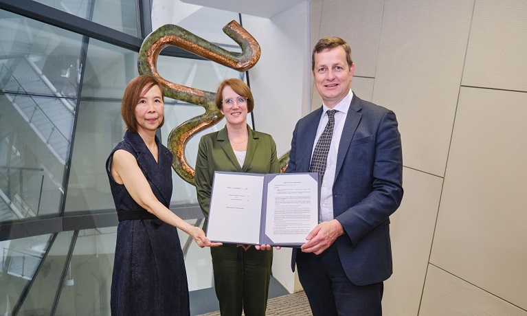 Two women and an man holding a folder open for the camera with a document displayed