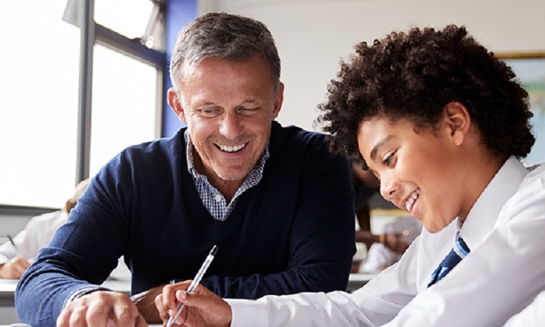 A smiling teacher helping a male pupil with their work