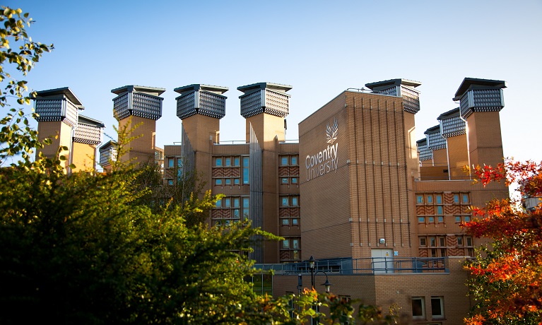 Coventry University's Lanchester Library with trees in the foreground and blue skies behind
