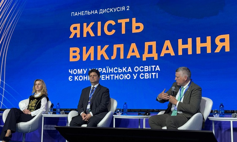 Sir Ciaran Devane sat in a chair speaking in to a microphone on stage at thie President's Forum in Kyiv