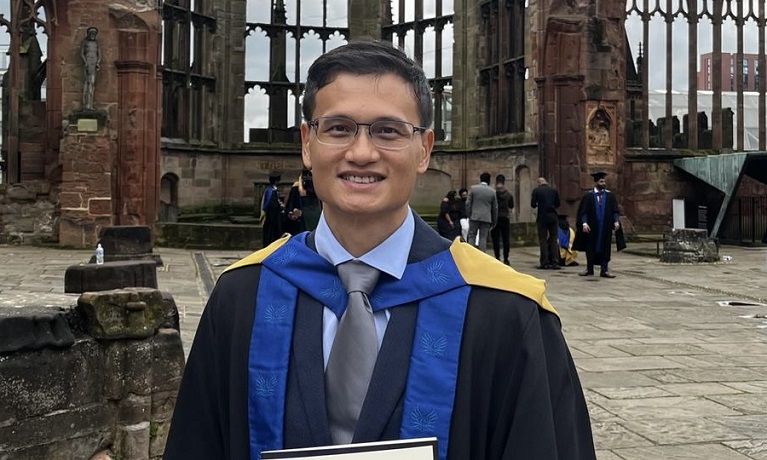 Daniel Ng in his graduation robes stood in the ruins of Coventry Cathedral