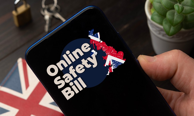 A moble phone being held in a hand showing the words 'Online Safety Bill'  alongside a map of Britain