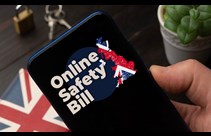 A moble phone being held in a hand showing the words 'Online Safety Bill'  alongside a map of Britain