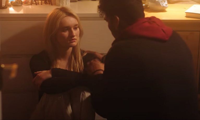 An image of a young women sitting on the floor with a young man putting his hand on her shoulder.