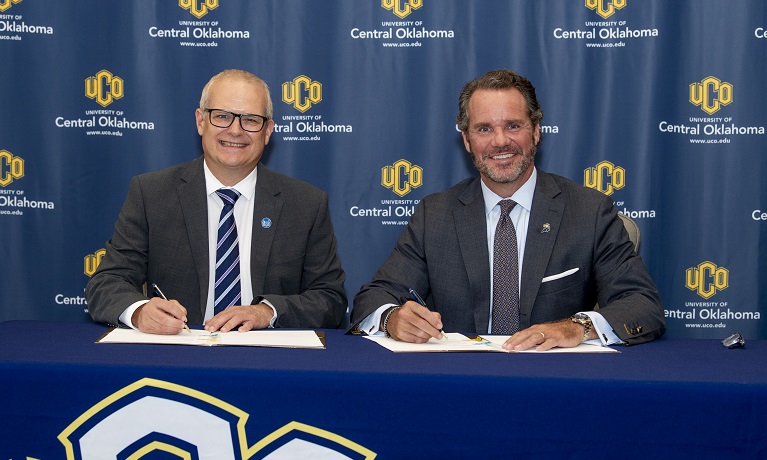 Richard Dashwood and President Todd G. Lamb seated at a table covered in a blue cloth holding pens ready to sign the agreement between Coventry University and the University of Central Oklahoma
