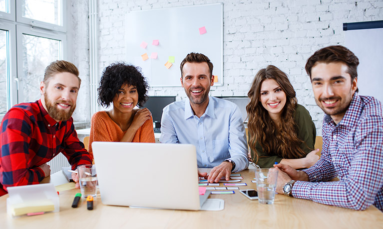 Five teachers sat around a table with a laptop in front of them, smiling at the camera.