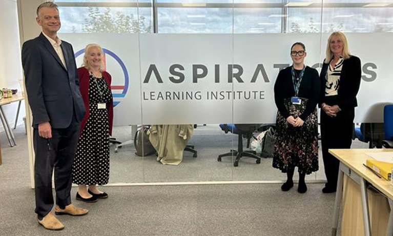 A group team photo in front of the Aspirations logo on the glass wall