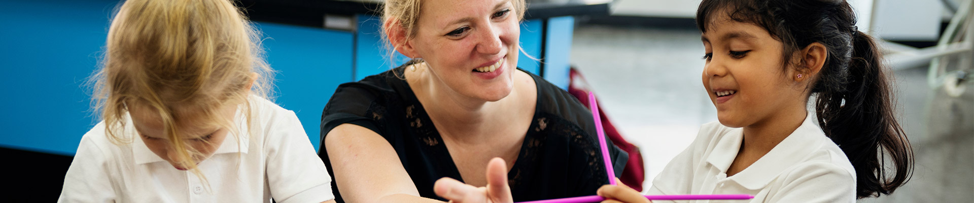 A woman teacher with blonde hair kneeling down next to a student using chemistry molecular models.