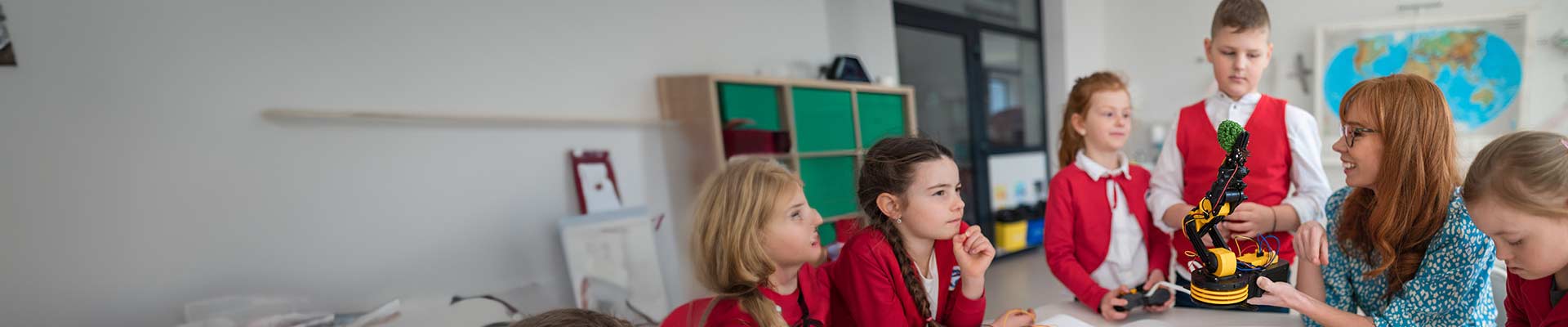 Teacher in a class room looking at a tablet standing beside a young school girl wearing a headset