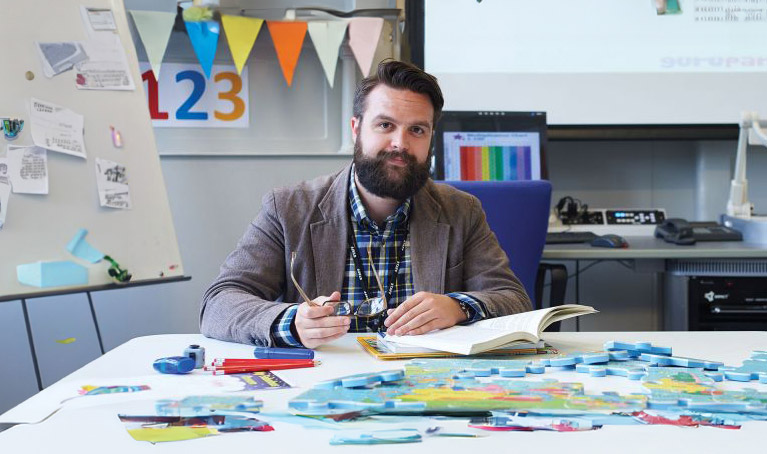 Matthew Tragheim sat in a classroom with a whiteboard behind him and colourful bunting.
