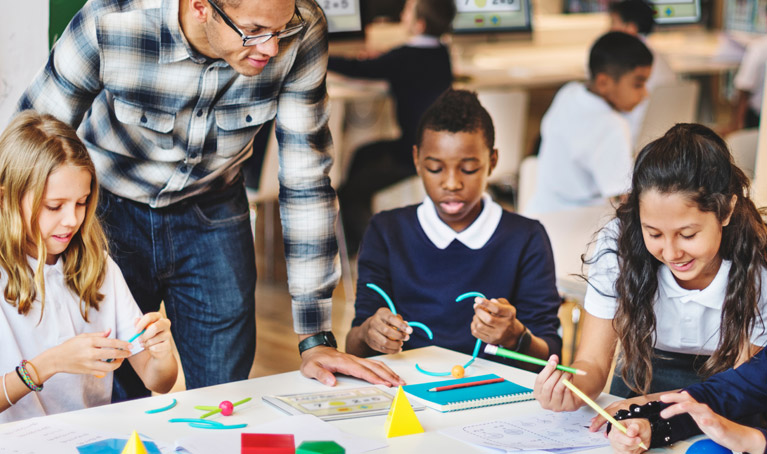 A teacher and students in the classroom sat around a large table, with materials in front of them