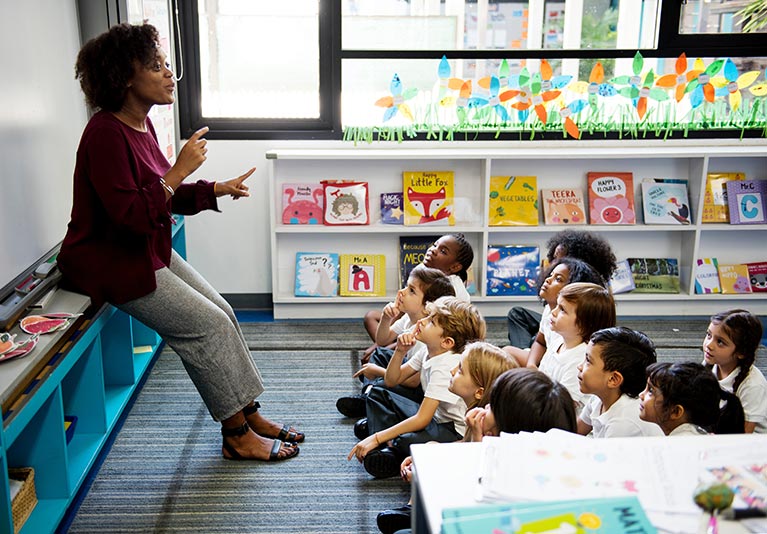 A teacher with a class of young students sat on the floor listening to her.
