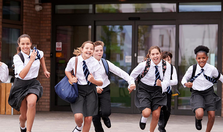 Children running out of school smiling wearing uniform