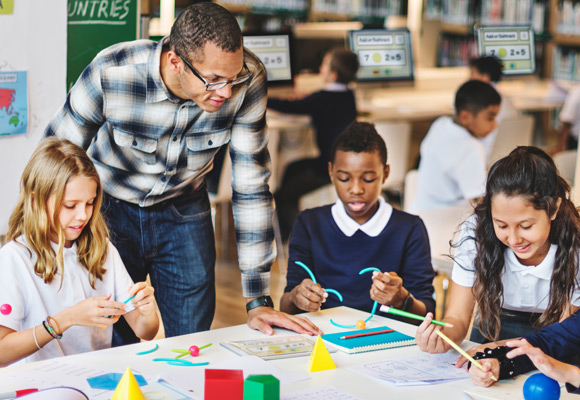 A teacher and students in the classroom sat around a large table, with materials in front of them