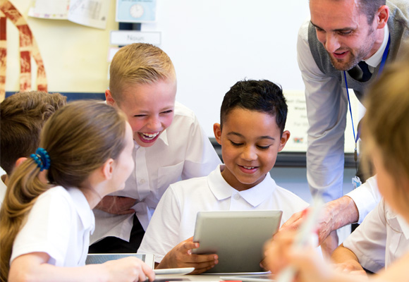 Young students sitting around a table while one holds a tablet.