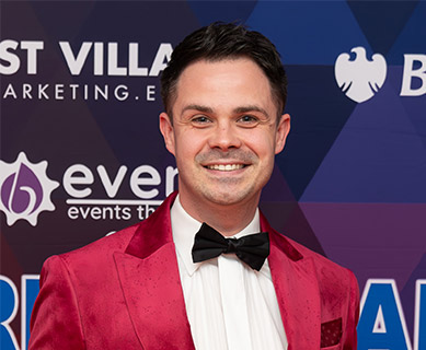 Chris Passey in a red suit against an event sponsor background.