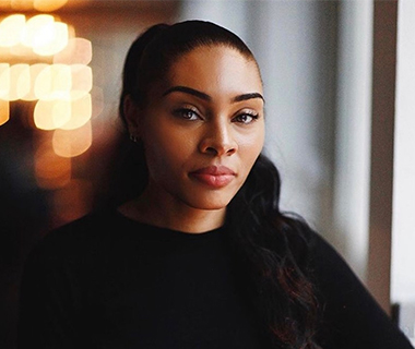 Portrait of Naomi against a blurred lit background.