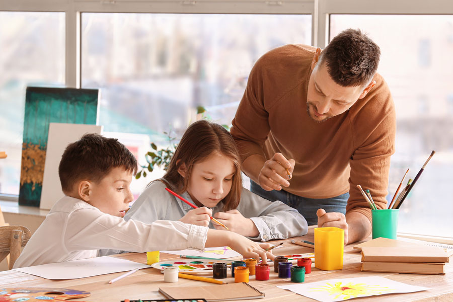 A young male teacher painting with young students in a classroom.