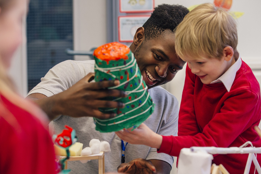 A young teacher with a student making a papier mache creature.