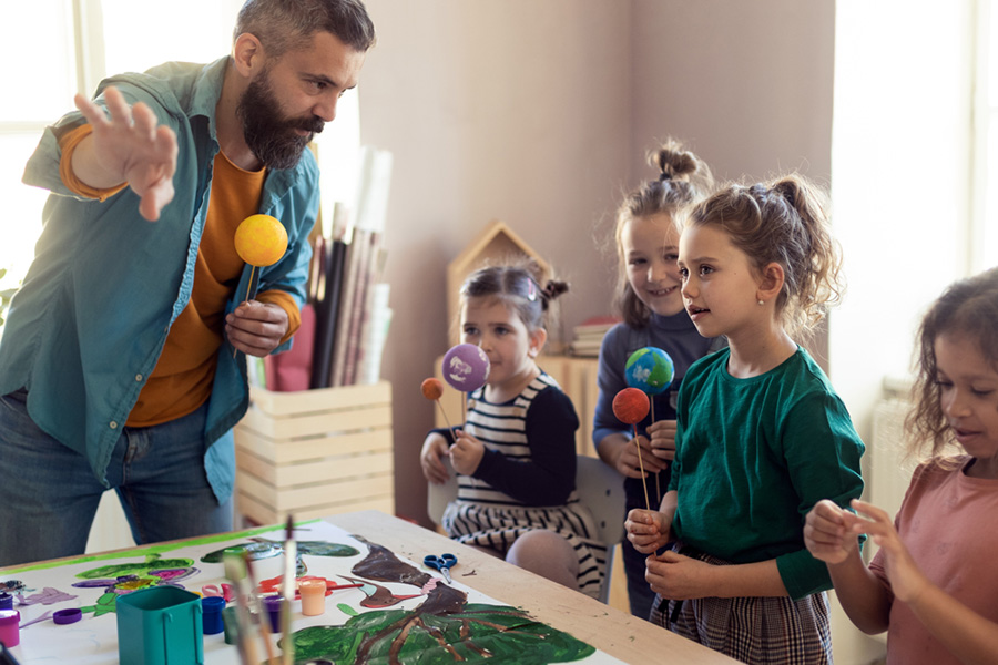 A male teacher with children in a classroom holding handmade planets on sticks.