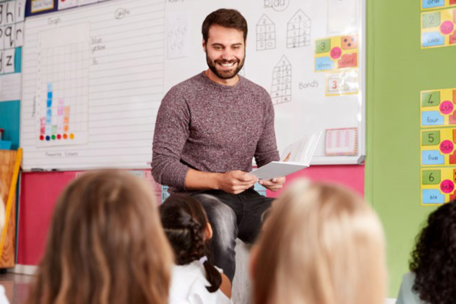 A teacher smiling as he stands up in front of a class of pupils.